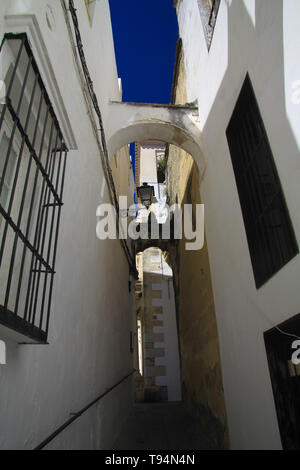 Basso angolo vista sulla stretto vicolo vuoto con facciate di case bianche e passi al piano di sopra in contrasto con il cielo blu scuro nel tradizionale villaggio spagnolo Arc Foto Stock