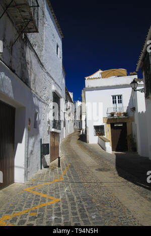 Luminoso e brillante vuoto isoalated stretto vicolo con ciottoli contro il profondo blu del cielo e tipico spagnolo case bianco - Arcos de la Frontera, Andalusia Foto Stock