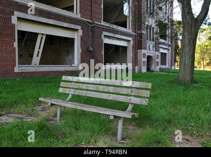Una panca in legno si siede di fronte a un pubblico abbandonato la scuola a Detroit, Michigan. Tutti della costruzione di porte e finestre sono state rotte o rimosso. Foto Stock