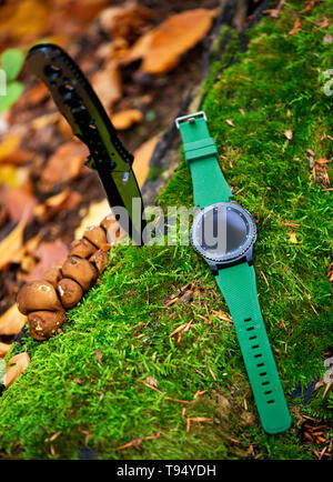 Set di maschi - coltelli e orologi. Coltello nero e smart watch in autunno forrest Foto Stock