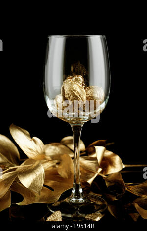 Wineglass con oro di noci e foglie su sfondo scuro Foto Stock