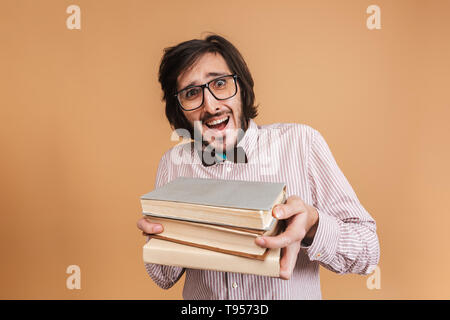 Immagine di funny nerd uomo 20s indossare occhiali e il filtro bow tie holding libri rimanendo isolate su sfondo beige in studio Foto Stock