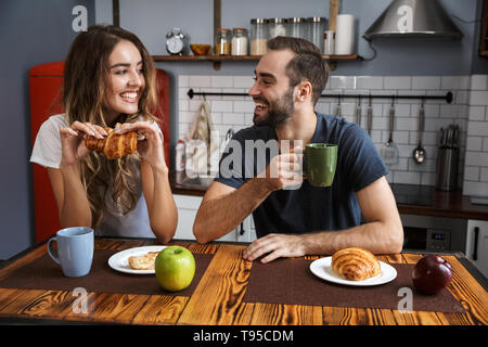 Ritratto di giovane caucasico l uomo e la donna di mangiare croissant mentre si consuma la colazione nella cucina elegante Foto Stock