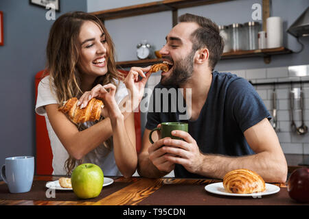 Ritratto di coppia attraente l uomo e la donna di mangiare croissant mentre si consuma la colazione nella cucina elegante Foto Stock