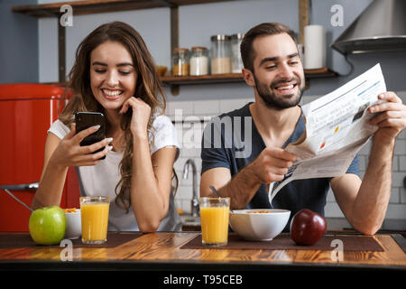 Ritratto di lieta giovane uomo e donna seduta al tavolo in cucina mentre si consuma la colazione a casa al mattino Foto Stock