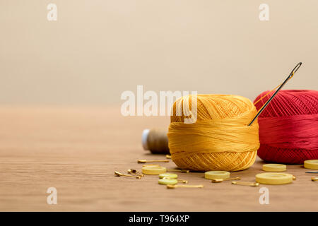 Cotone filato per maglieria sfere con pulsanti di abbigliamento e le spine di sicurezza sul tavolo di legno isolata sul beige con spazio di copia Foto Stock