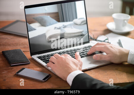 Aziendali di man mano sul tavolo utilizzando un computer portatile con hotel Prenotazione di camera Foto Stock