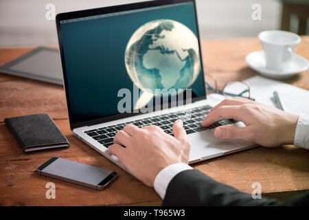 Aziendali di man mano sul tavolo utilizzando un computer portatile con globo sullo schermo Foto Stock