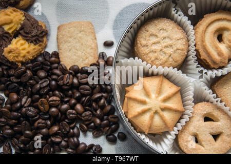 I biscotti con lo zucchero in una scatola rotonda, ripartito con carta e con i chicchi di caffè spruzzata su di una tovaglia Foto Stock