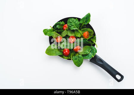 Il verde di spinaci freschi foglie con cur pomodorini in padella su sfondo bianco Foto Stock