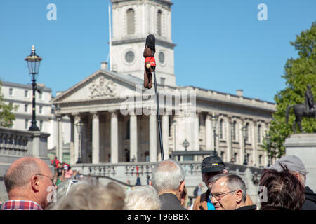 La guida turistica di pensionati leader su un tour a piedi attorno a Trafalgar Square con un lungo bastone e una piccola figura attaccato su un giorno caldo e soleggiato in primavera. Foto Stock