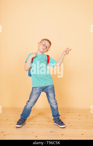 Piccolo ragazzo divertente stare in studio con occhiali, zaino. Sorprendente. Isolati in giallo. Scuola di concetto Foto Stock