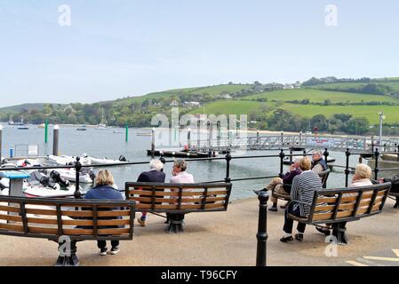 La gente seduta sulle panchine godendosi la vista su tutta la foce a Salcombe waterfront su una giornata d'estate,Devon England Regno Unito Foto Stock