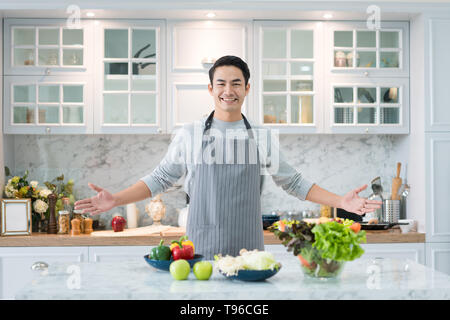 Asian uomo bello la cottura a casa a preparare insalata in cucina. Mangiare sano, cibo vegetariano, dieta e concetto di persone Foto Stock