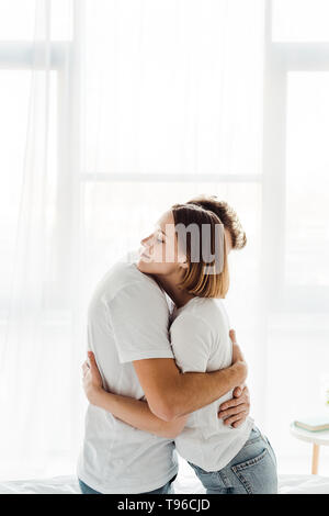 Coppia romantica in bianco t-shirts abbracciando a casa Foto Stock