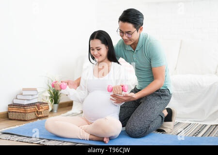 Bella donna incinta facendo esercizio con manubri con mio marito aiutare sua moglie a casa sano concetto Foto Stock