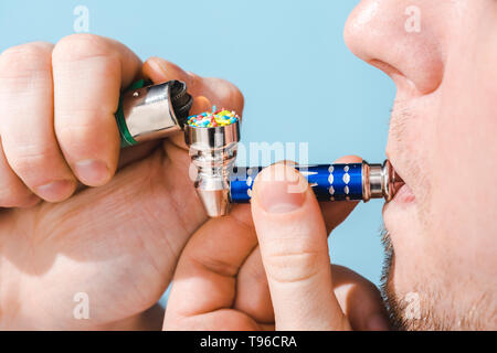 Vista ritagliata dell uomo di illuminazione tubo di fumo con colorati spruzza isolato sul blu, zucchero concetto di dipendenza Foto Stock