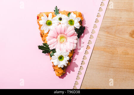 Vista superiore del trancio di pizza con fiori su carta rosa con tagliare fuori i cuori sul tavolo di legno Foto Stock