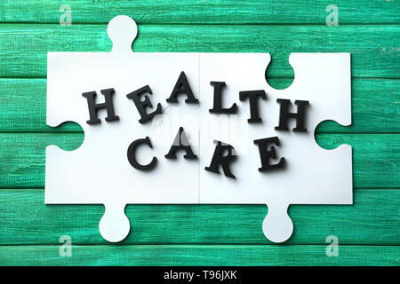 Testo HEALTH CARE fatta di lettere scuro con i pezzi di un puzzle sul colore di sfondo in legno Foto Stock