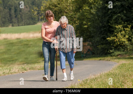 Giovane donna aiutando senior lady con bastone Foto Stock