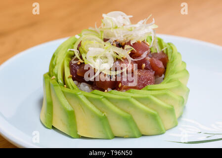 Tartare di tonno rosso carne su un letto di riso, guarnite con fette di avocado e sottili fette di porri, in bianco e nero salsa di sesamo su un bianco p Foto Stock