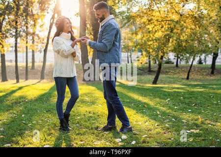 Giovane uomo mettendo anello di fidanzamento sulla fidanzata del dito in autunno park Foto Stock