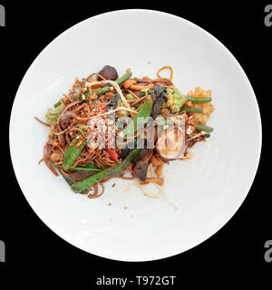 Tagliatelle di grano saraceno con verdure e funghi nel piatto rotondo isolato su sfondo nero Foto Stock