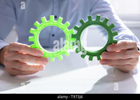 Imprenditore unendo insieme ingranaggi sul tavolo di legno al posto di lavoro Foto Stock