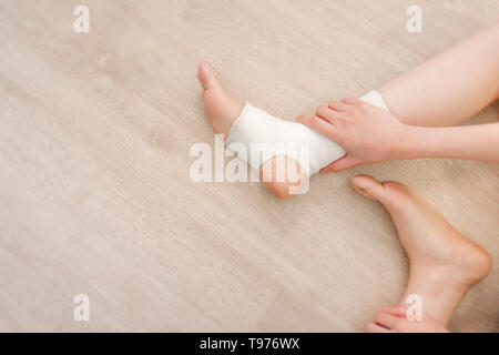 Primo piano il popolo di un piede con il Bianco di garza bendaggio elastico. Mani sui feriti gambe e piedi sulla zona del dolore. Asian giovane donna lesioni della caviglia Runner seduta Foto Stock