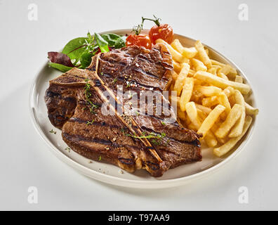 Grigliata di T-bone steak con de pommes frites e verdure fresche aromatizzati con erbe e servita su una piastra su bianco per menu pubblicità Foto Stock