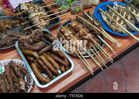 Cibi di strada in Laos, scelto focus, Grill. Diversi tipi di carne di pesce e altri prodotti alimentari sul contatore sul tavolo. Cucina di strada in Asia. Foto Stock