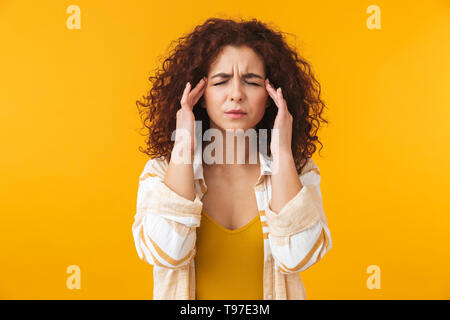 Immagine della donna tesa 20s con capelli ricci strofinando il templi a causa di mal di testa, isolate su sfondo giallo Foto Stock