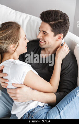 Immagine del giovane in amore uomo e donna abbracciando insieme seduti sul divano nella luminosa sala a casa Foto Stock