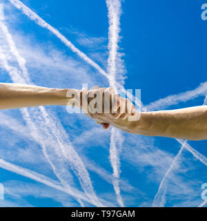 Primo piano di un uomo e una donna si stringono la mano sopra il bello blu cielo con contrails. Foto Stock