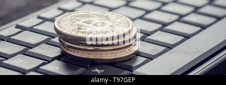 Effetto retrò sbiadito e tonica immagine di una delle quattro bitcoins su una tastiera nera in ampia vista panoramica. Foto Stock