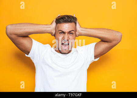 Immagine del ragazzo arrabbiato 30s in t-shirt bianca con urla e testina di afferraggio isolate su sfondo giallo Foto Stock