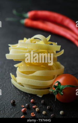 Su sfondo nero in sfere di materie fettuccine con pomodori freschi con radici, il rosso e il nero di pepe e due cialde di peperoncino Foto Stock