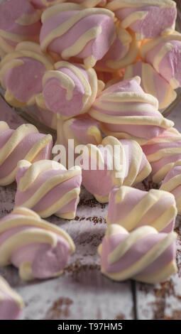 Rosa marshmallows con riccioli di bianco ottenendo abbastanza sonno con un contenitore trasparente sul vecchio di luce sullo sfondo di legno Foto Stock