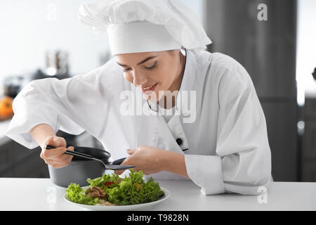 Giovani chef femmina di condimento per insalata gustosa in cucina Foto Stock