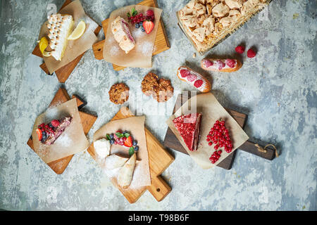 Un assortimento di dolci: torta, churos, rotolo di meringa, gelato, decorata con frutti di bosco su tavole di legno. Vista dall'alto. Grigio sfondo a trama. Bellissimi piatti di servizio. Il dessert. La catena alimentare Foto Stock