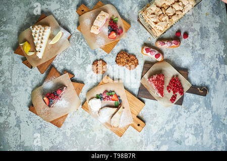 Un assortimento di dolci: torta, churos, rotolo di meringa, gelato, decorata con frutti di bosco su tavole di legno. Vista dall'alto. Grigio sfondo a trama. Bellissimi piatti di servizio. Il dessert. La catena alimentare Foto Stock