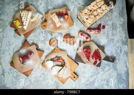 Un assortimento di dolci: torta, churos, rotolo di meringa, gelato, decorata con frutti di bosco su tavole di legno. Vista dall'alto. Grigio sfondo a trama. Bellissimi piatti di servizio. Il dessert. La catena alimentare Foto Stock