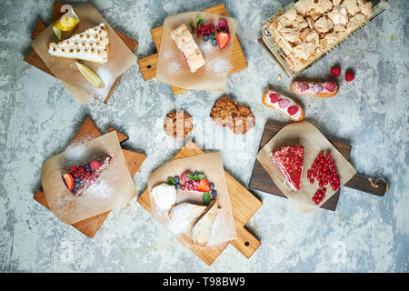 Un assortimento di dolci: torta, churos, rotolo di meringa, gelato, decorata con frutti di bosco su tavole di legno. Vista dall'alto. Grigio sfondo a trama. Bellissimi piatti di servizio. Il dessert. La catena alimentare Foto Stock