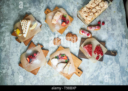 Un assortimento di dolci: torta, churos, rotolo di meringa, gelato, decorata con frutti di bosco su tavole di legno. Vista dall'alto. Grigio sfondo a trama. Bellissimi piatti di servizio. Il dessert. La catena alimentare Foto Stock