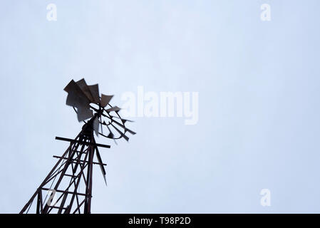 Un vecchio mulino a vento di ferro in una fattoria in western New South Wales, gira nel vento su un nuvoloso cielo grigio giorno e pompe acqua da un sub foro artesiano Foto Stock