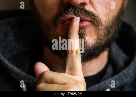 Per non parlare, essere tranquillo - close up ritratto di uomo barbuto sulla porta dicendo shhh. Il dito sulle labbra. Testa e spalle, senza occhi. Pericolo. Foto Stock