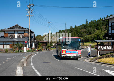 Uomo a salire su un autobus alla fermata del bus di Magome-juku, Nakatsugawa, Giappone con una locanda, foresta, elettricità cavi e cielo blu in background. Foto Stock