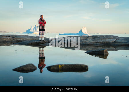 Inuit donna in abiti tradizionali sorge sulle rive della baia di Disko su Midsummer, Groenlandia Foto Stock