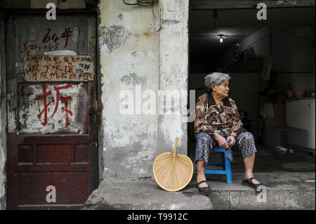 02.08.2012, Chongqing, , Cina - Una vecchia donna è seduta sui gradini davanti alla sua casa nella città vecchia di Chongqing. In corrispondenza della porta dipinta charact Foto Stock