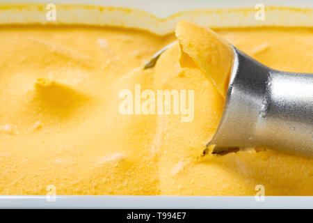 Vista laterale cucchiaio tenuto fuori il sapore di mango gelato Foto Stock